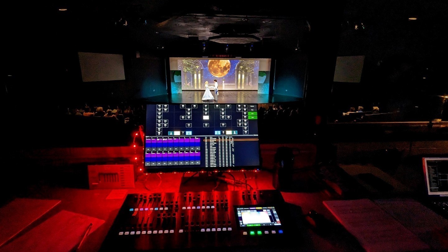 The theater light board with Cinderella the musical being performed on stage in the background.