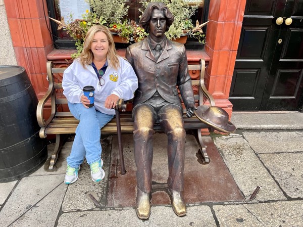 Noel Loveland sitting with bronze statue of Oscar Wilde.